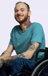 Homem jovem tatuado em uma cadeira de rodas sorrindo para a camera